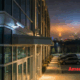 Exterior of a modern commercial building at night with security lighting and visible surveillance coverage overlooking a parking area.