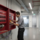 Technician inspecting a commercial fire alarm control panel explaining why fire alarms need to be replaced