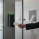 A sleek smart credential reader mounted on a modern glass and metal office door in Atlanta, glowing with a soft green light to indicate authorized entry.